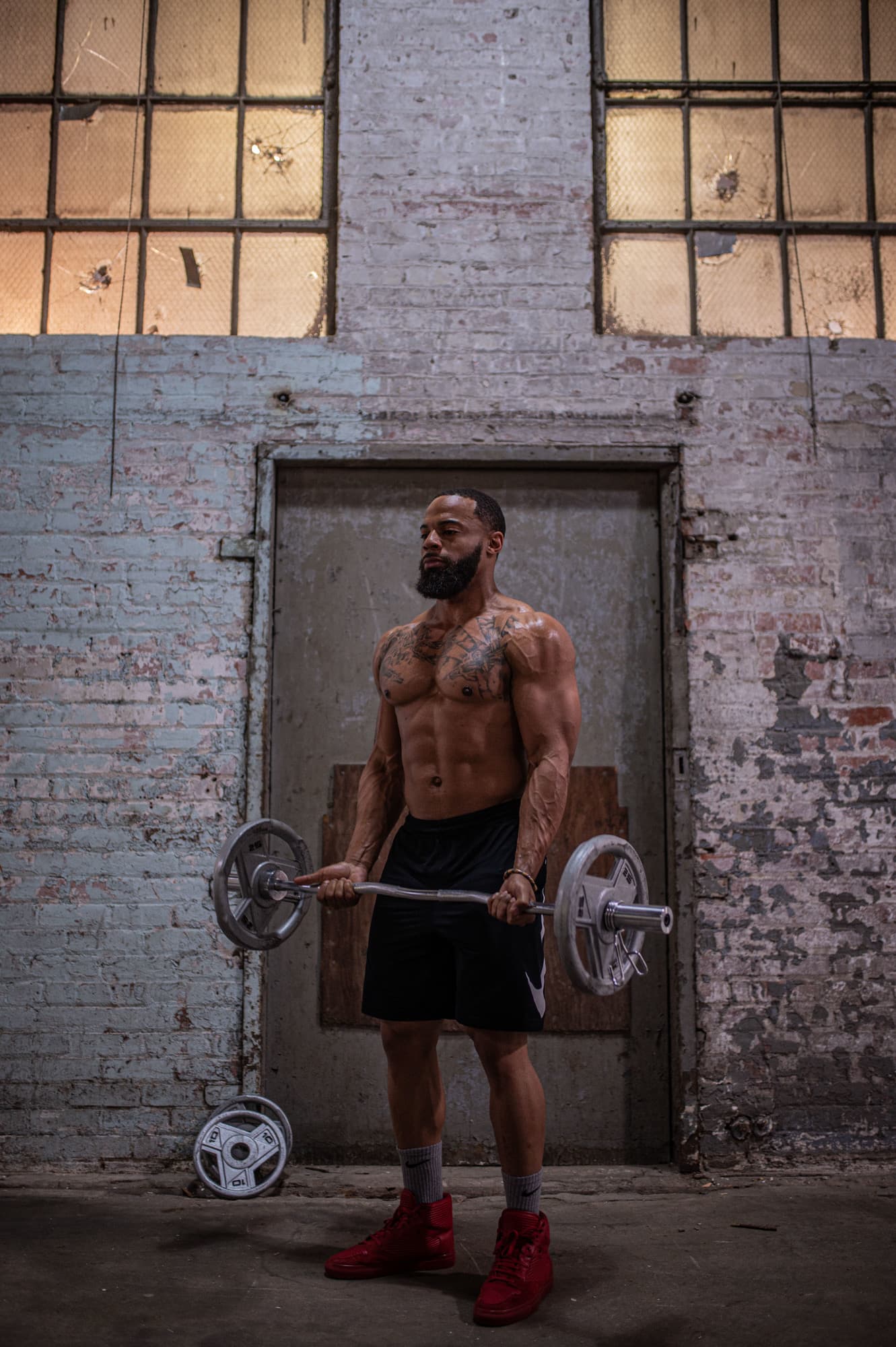 Chris Frazier curling an EZ bar in a brick warehouse gym