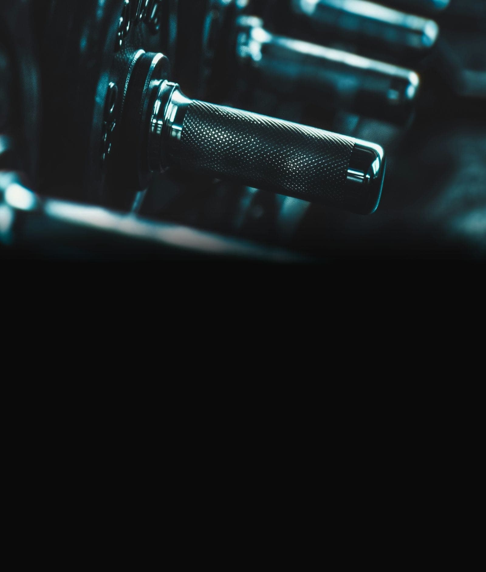 Close-up of a dumbbell's knurled handle in a dimly lit rack of dumbbells