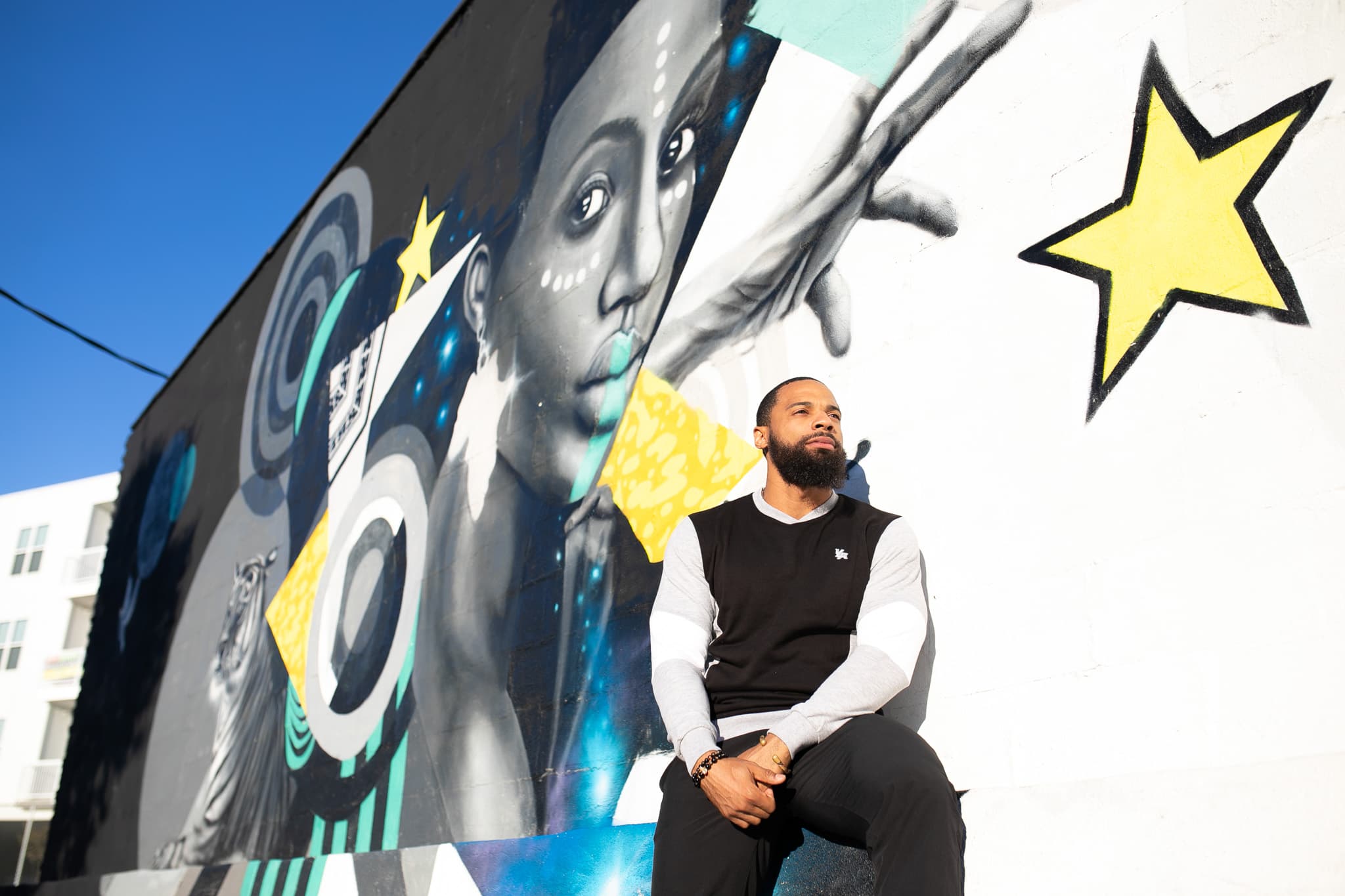 Chris Frazier seated on a wall beneath a large mural